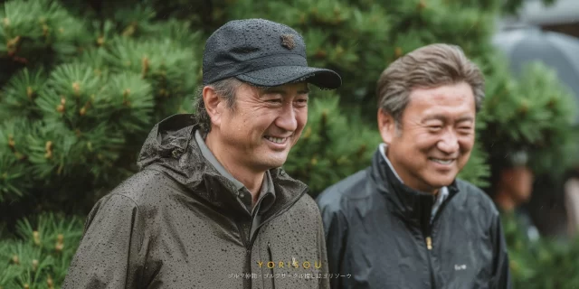 広島市安佐北区可部町のゴルフ場で雨天の中でも笑顔で会話を楽しむ中高年男性ゴルファー仲間の自然な様子