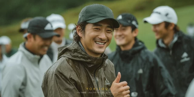 和歌山市加太のゴルフ場で、雨上がりのラウンド中にゴルフウェア姿の30代男性ゴルファーが仲間に囲まれて笑顔で親指を立てているバストアップ写真