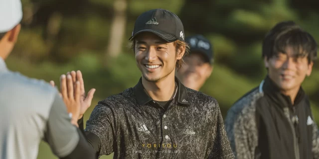 八戸市根城エリアのゴルフ場で、ゴルフウェア姿の30代男性ゴルファーが仲間とハイタッチを交わしているバストアップの様子。ラウンド中の自然な笑顔と、近い生活圏同士の気軽な関係性が伝わる雰囲気。