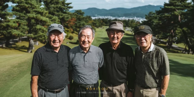 中央区佃・月島エリアから参加したシニア男性ゴルファー4人が、自然に囲まれたゴルフ場で穏やかな表情を浮かべて並んでいる様子