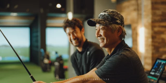 インドアゴルフでコーチと会話しながら体験練習を楽しむシニアゴルファー